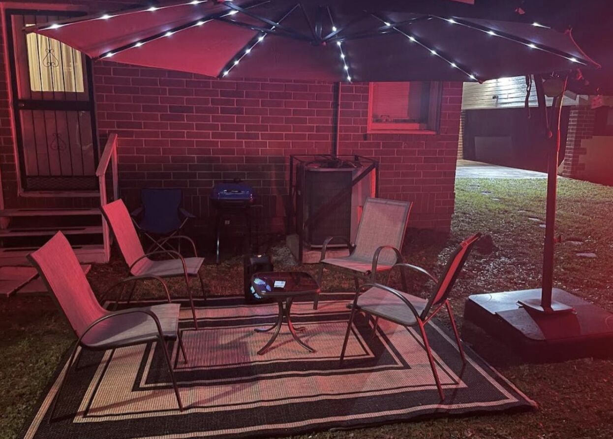 An outdoor patio with a brick wall, a red umbrella, and several chairs.