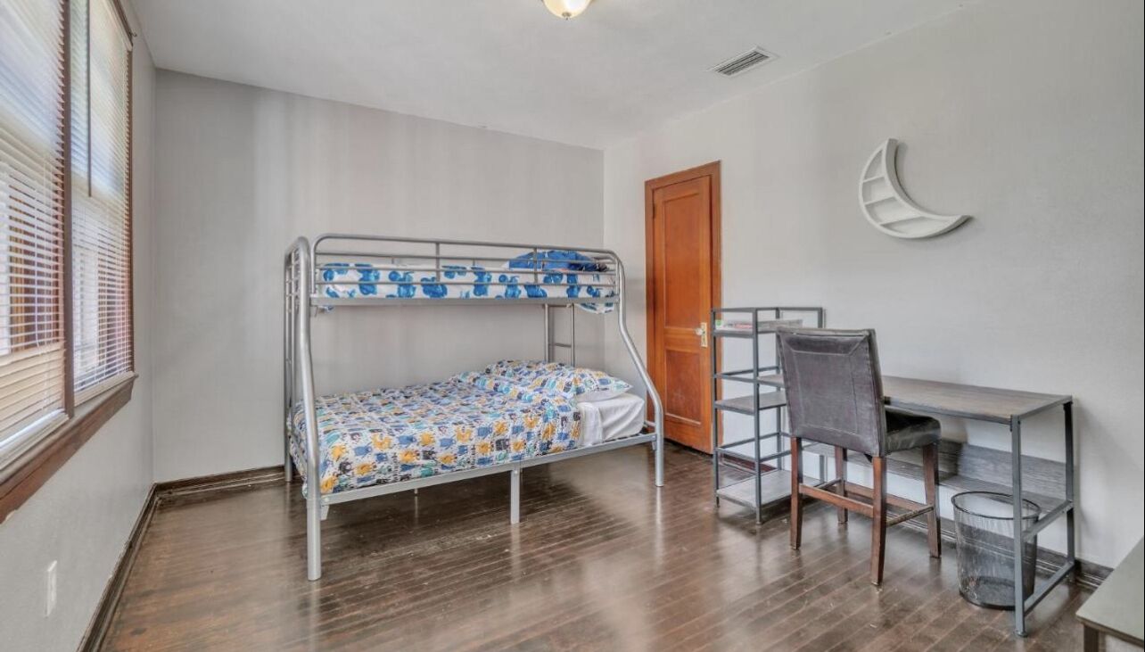 Una cama litera con una colcha estampada, un escritorio con una silla y una decoración con forma de luna creciente en la pared.