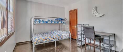Una cama litera con una colcha estampada, un escritorio con una silla y una decoración con forma de luna creciente en la pared.