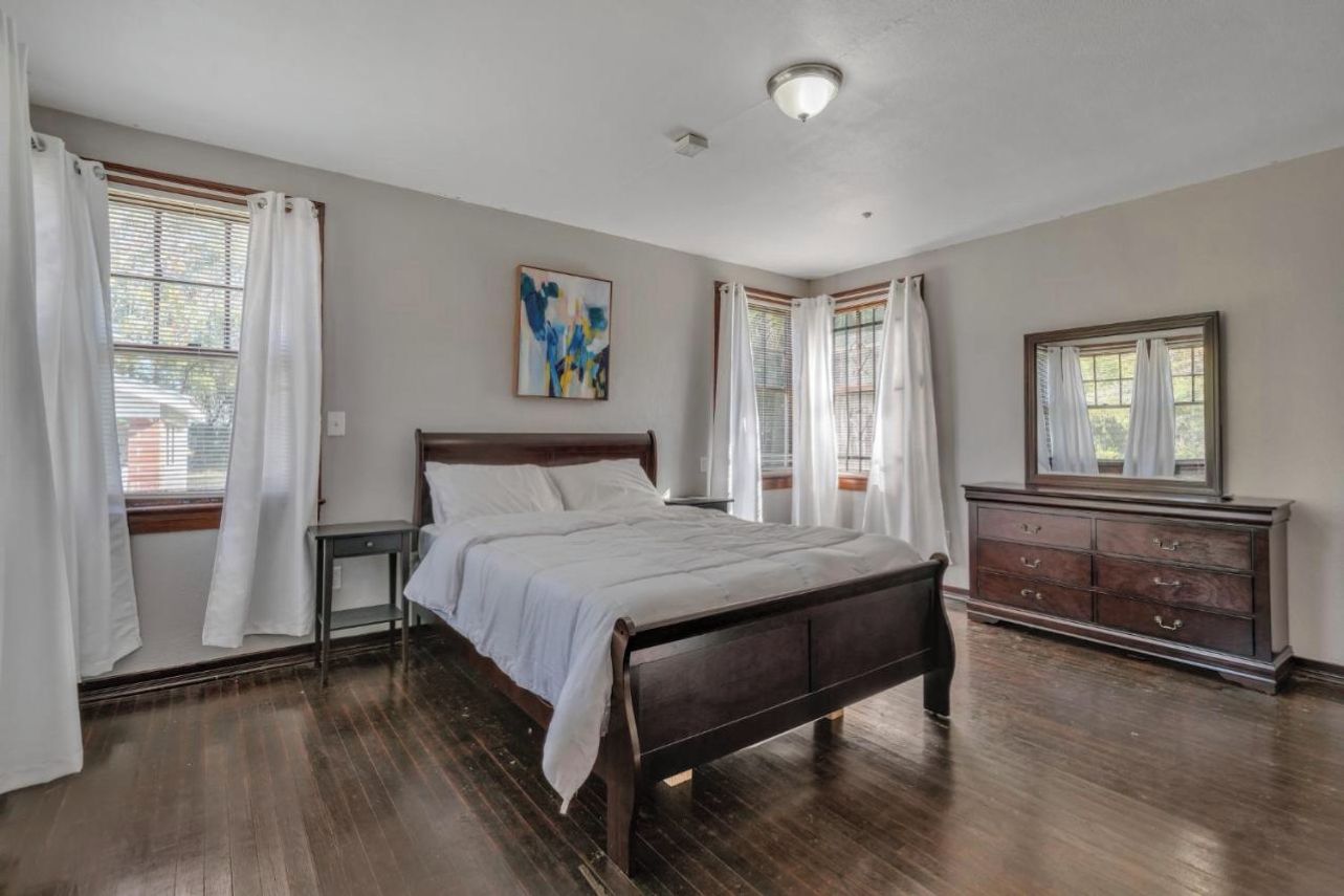 Un dormitorio con una cama de madera, cortinas blancas, un aparador y un cuadro en la pared.