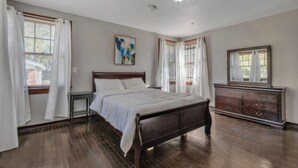 A bedroom with a wooden bed, white curtains, a dresser, and a painting on the wall. - Comfy pet friendly home in JAX mins to downtown (Jacksonville)