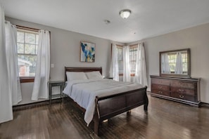 A bedroom with a wooden bed, white curtains, a dresser, and a painting on the wall. - Comfy pet friendly home in JAX mins to downtown (Jacksonville)
