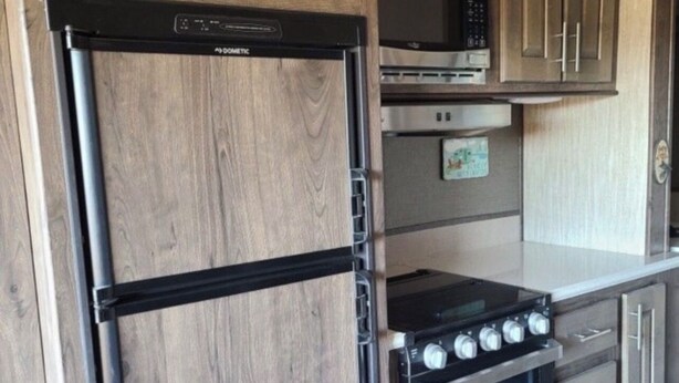 Une cuisine compacte dotée d’un réfrigérateur, d’une cuisinière, d’un four à micro-ondes et de meubles de rangement en bois intégrés.