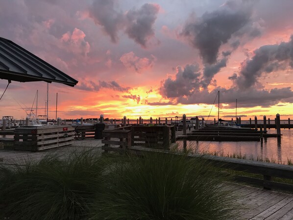 A marina at sunset with boats docked, wooden walkways, and a grassy foreground.