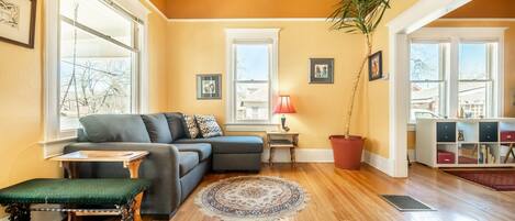 A cozy living room with a sectional sofa, a small table, a bench, and a large potted plant.