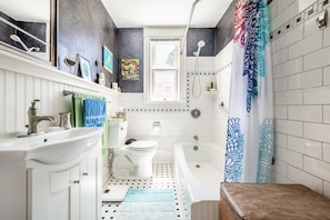 A bathroom with a white sink, toilet, and bathtub. There are towels hanging on the wall, a shower curtain, and a window above the toilet. - Mt Washington House (Colorado Springs)