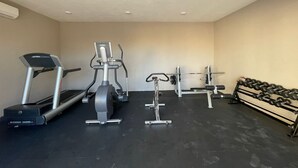 A gym with a treadmill, elliptical, weight bench, and dumbbells.