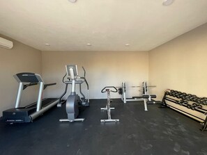 Un gimnasio con cinta de correr, elíptica, banco de pesas y mancuernas.