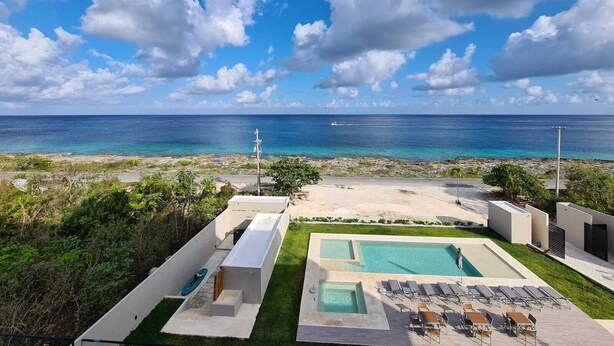 A resort with a pool area, lounge chairs, and a view of the ocean.