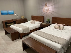 Habitación de hotel con dos camas, un escritorio, una silla y un banco.