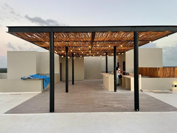 An outdoor terrace with a wooden pergola, a reception desk, and a view of the sky.