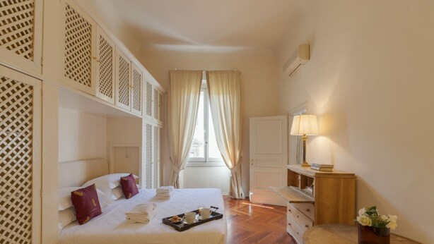 A hotel room with a bed, a desk, a lamp, and a window with curtains. - Raso cozy penthouse near the Duomo (Firenze)