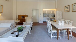 A modern living room with a sofa, coffee table, and dining table. There is a kitchen in the background with a refrigerator and cabinets. - Raso cozy penthouse near the Duomo (Firenze)