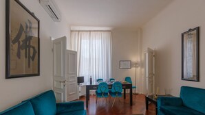 A living room with teal sofas, a dining table with chairs, a TV, and a large framed artwork on the wall. - Seta spacious apartment next to the Duomo (Firenze)