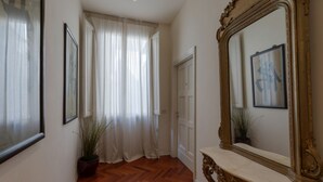Een hal met een houten vloer, een grote spiegel met een sierlijk frame en een deur naar een andere kamer.