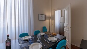 A dining area with a table set for four, including plates, glasses, cutlery, and a bottle of wine. There are two chairs, one blue and one teal, and a floor lamp is visible. - Seta spacious apartment next to the Duomo (Firenze)