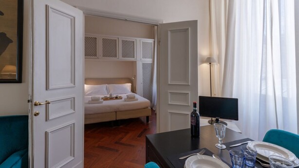 A hotel room with a bed, a desk with a computer, a bottle of wine, and a window with curtains. - Seta spacious apartment next to the Duomo (Firenze)