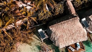 An aerial view of a beach resort with overwater bungalows, clear turquoise waters, and lush tropical vegetation.