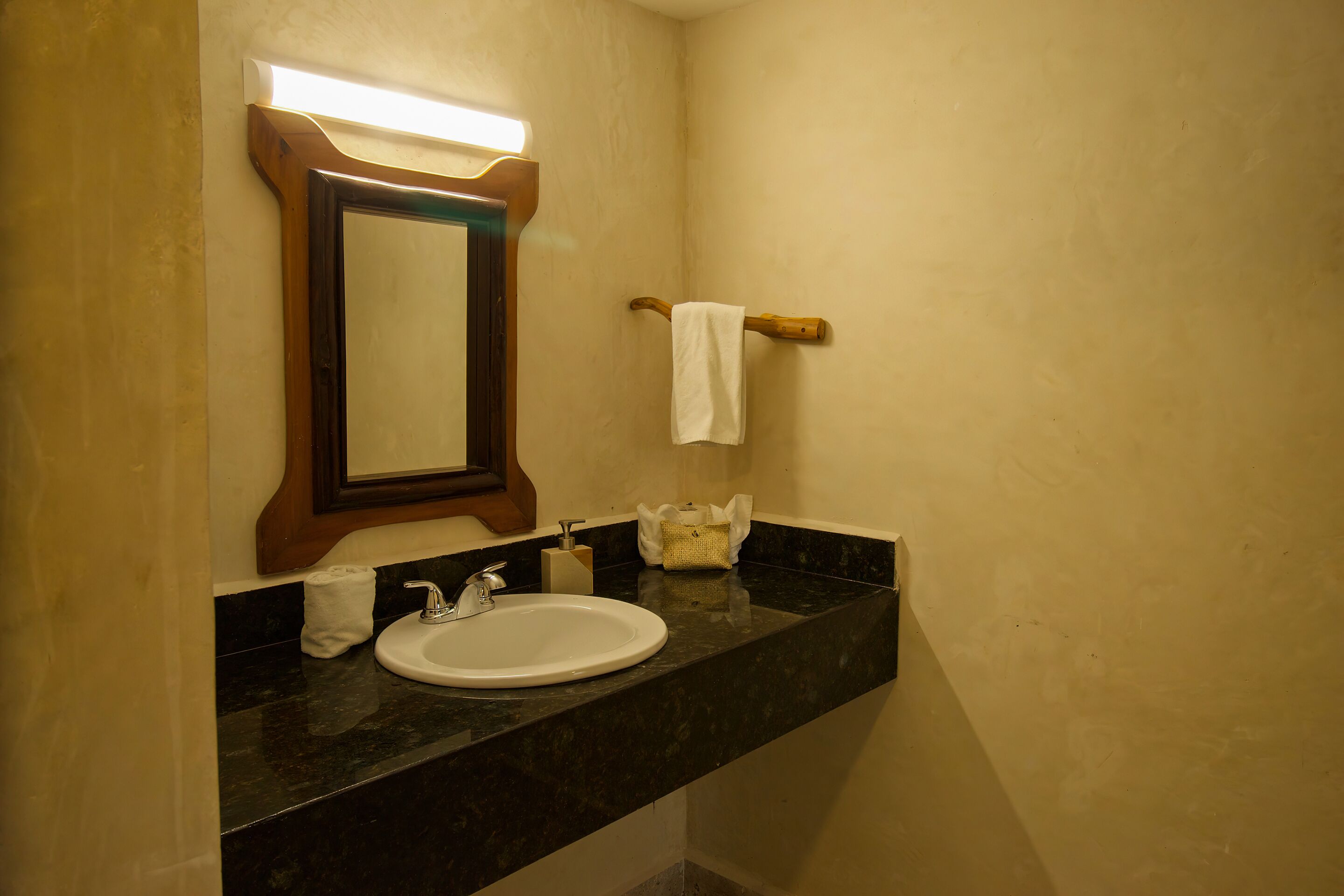 A bathroom with a sink, mirror, towel rack, and a soap dispenser.