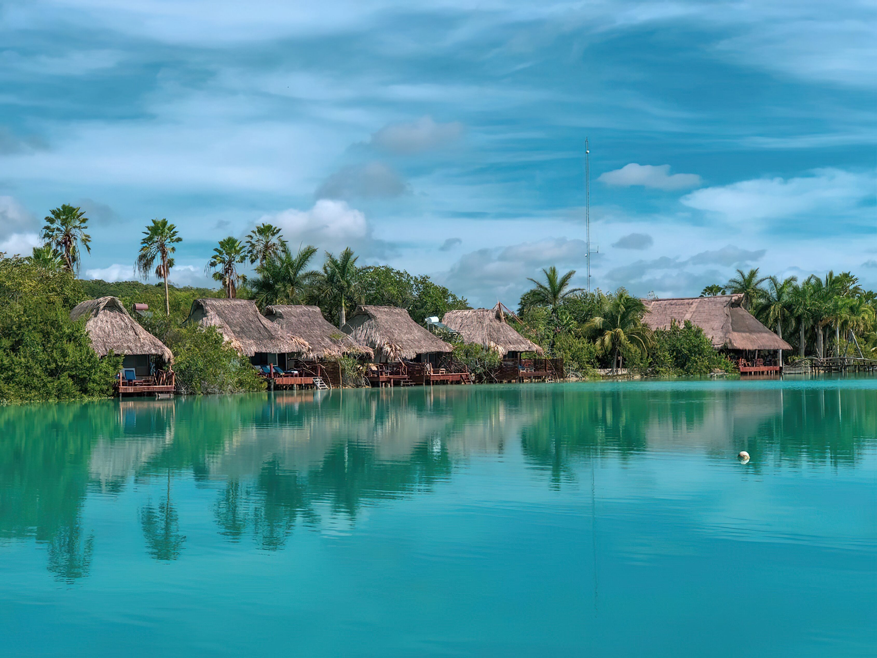 A resort with thatched-roof bungalows by a turquoise lagoon, surrounded by lush greenery.