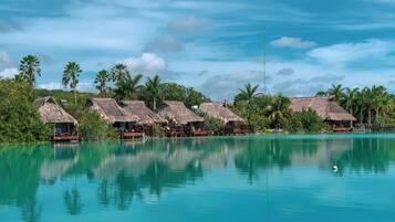 A resort with thatched-roof bungalows by a turquoise lagoon, surrounded by lush greenery.
