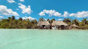 A beachfront property with thatched-roof huts, clear turquoise water, and palm trees.