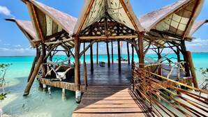 A wooden pier leading to a thatched-roof structure with a view of the turquoise sea.