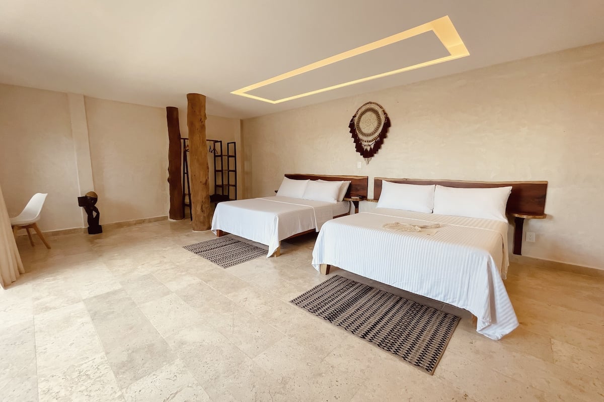 A hotel room with two beds, a chair, a wooden column, and a wall-mounted decorative piece.