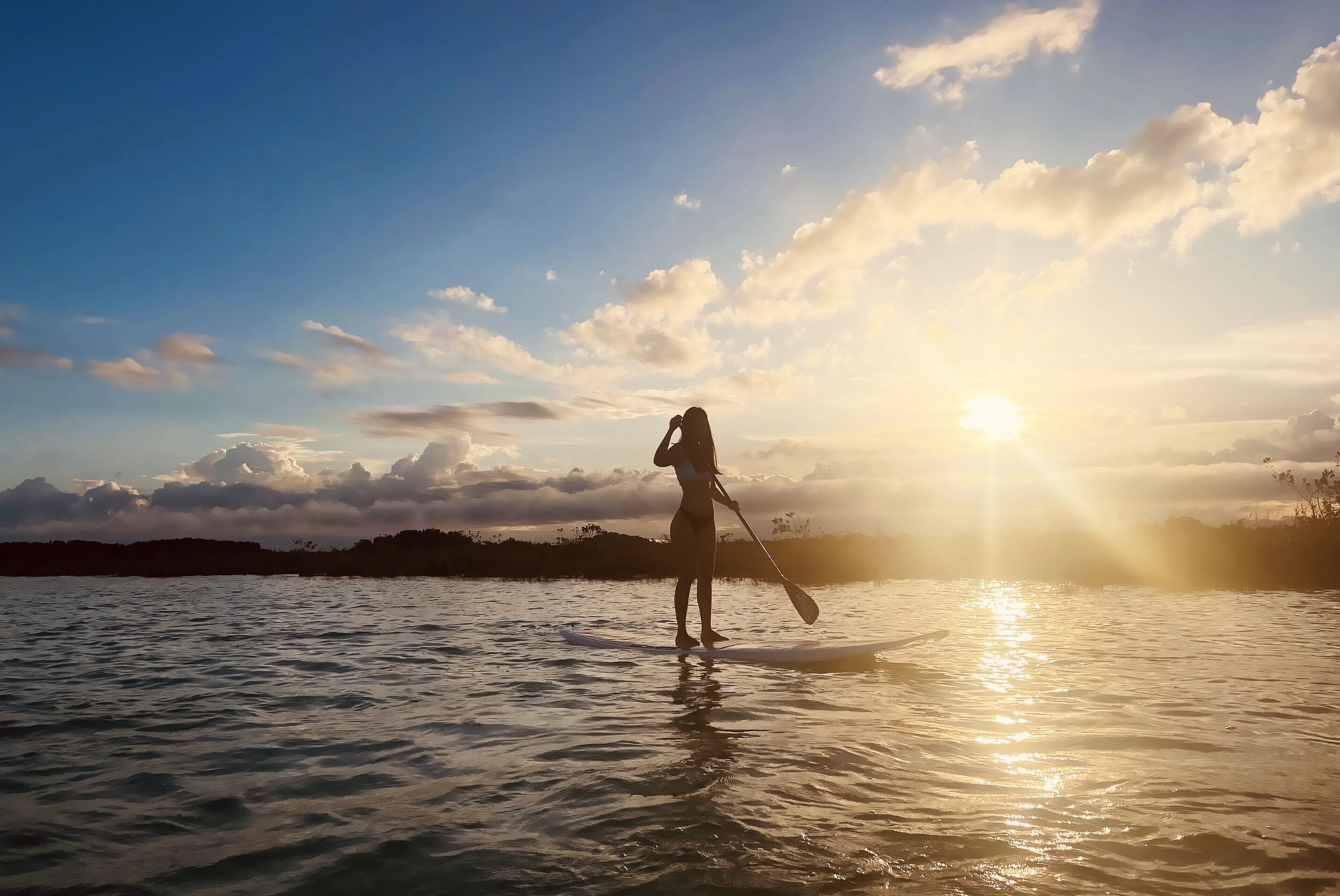 Una persona haciendo paddleboard sobre aguas tranquilas al atardecer.
