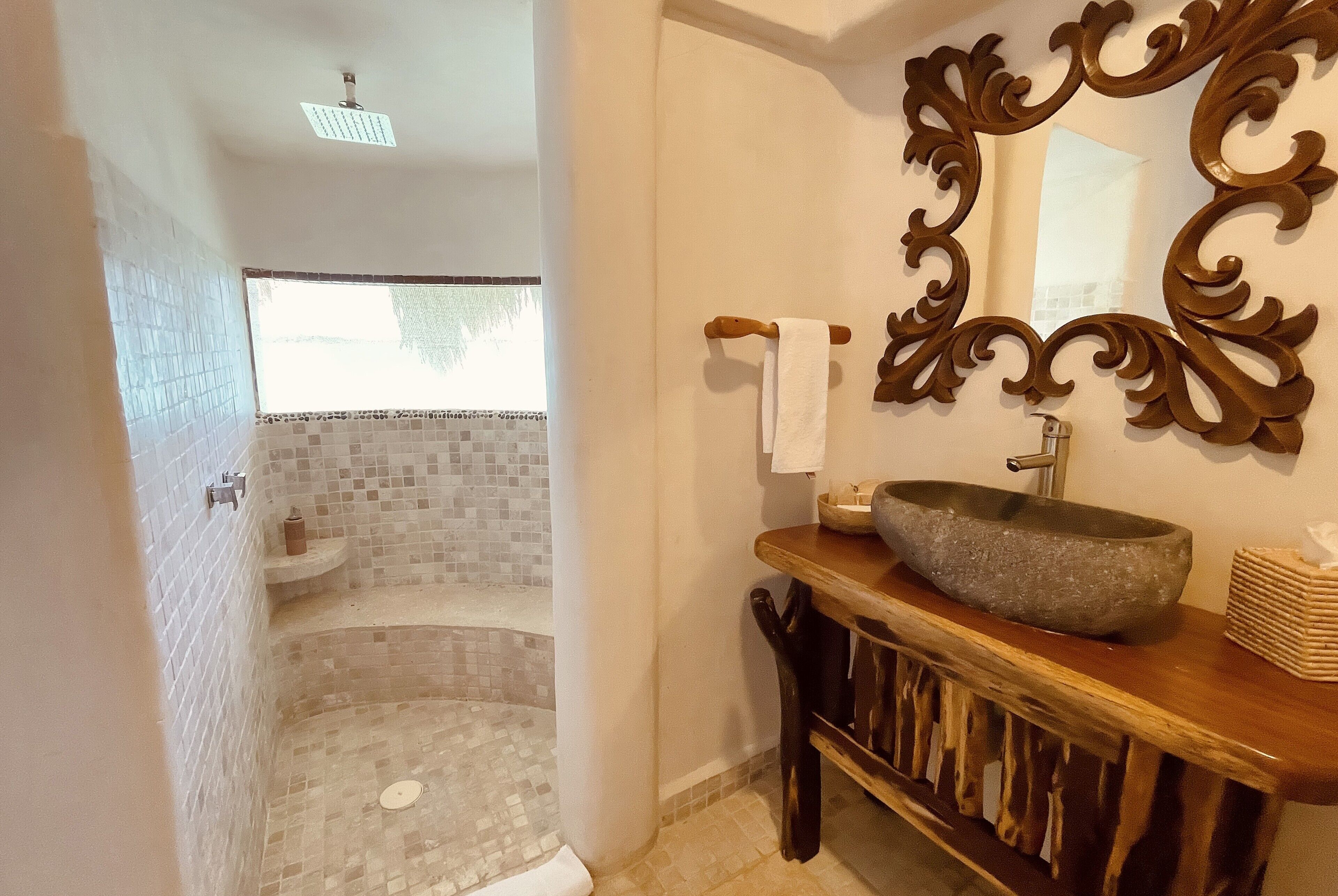 A bathroom with a bathtub, a shower, a sink with a stone basin, a decorative mirror, and a wooden vanity.