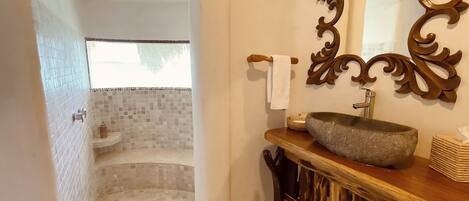 A bathroom with a bathtub, a shower, a sink with a stone basin, a decorative mirror, and a wooden vanity.