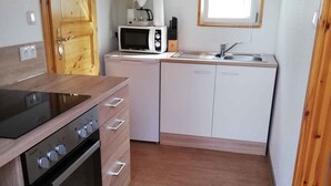 Een kleine keuken met een fornuis, magnetron, spoelbak en houten keukenkastjes.