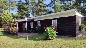 Een houten chalet met een overdekte veranda, omringd door een verzorgd gazon en bloeiende planten.