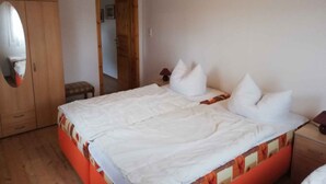 Een slaapkamer met een houten plafond, een bed met witte beddengoed, een houten kledingkast en een klein tafeltje met een lamp.