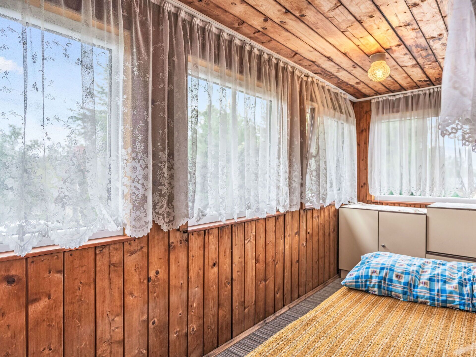 Una habitación con paredes de madera, una cama con manta escocesa y cortinas traslúcidas en las ventanas.