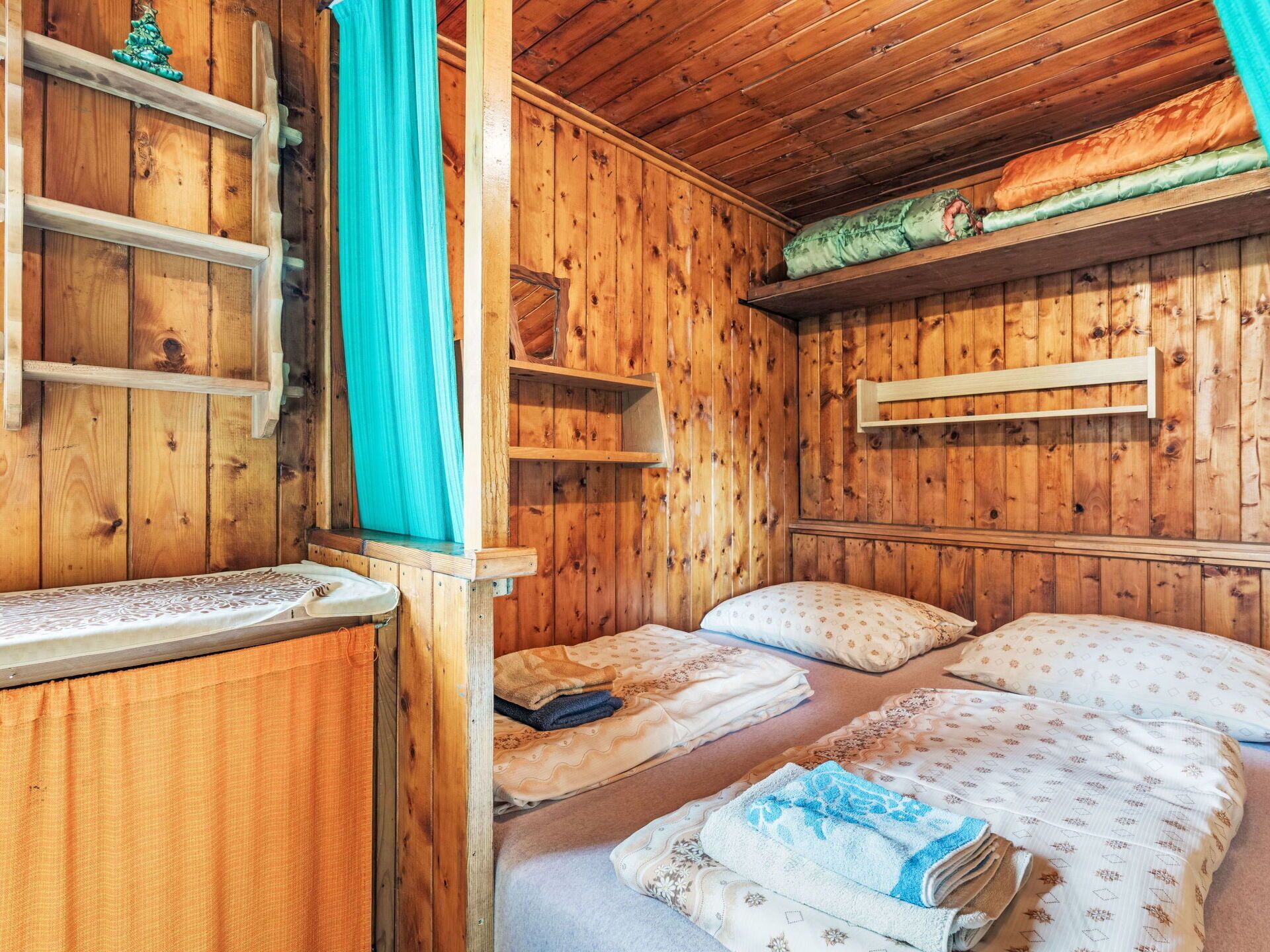 Una habitación de cabaña de madera con dos camas, un estante pequeño y una ventana con cortina.