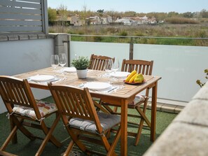 Een houten tafel voor vier personen met stoelen, een bloempot en een schaal met fruit.