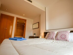 Een hotelkamer met een groot bed, een kledingkast, een spiegel en een nachtkastje met een lamp.