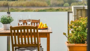 A wooden table with two wine glasses and a fruit bowl, a potted plant, and a view of a field and trees. - Beautiful apartment for 4 people with WIFI, pool, TV, terrace and pets allowed (Empuriabrava)