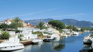 A marina with boats docked along a waterfront, surrounded by buildings and mountains in the background. - Beautiful apartment for 4 people with WIFI, pool, TV, terrace and pets allowed (Empuriabrava)