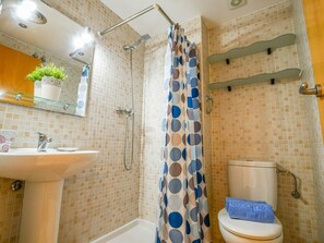 Een badkamer met douche, toilet, wastafel en spiegel.