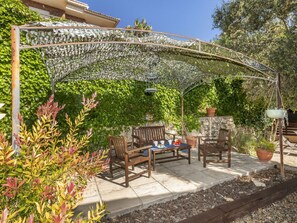 Eine Terrasse mit Holztisch und -stühlen, umgeben von einer Pergola, die mit Kletterpflanzen bewachsen ist.