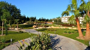 A landscaped garden with palm trees, a pathway, and a building in the background. - Beautiful apartment for 4 people with pool, A/C, TV and terrace (Sant Carles De La Ràpita)