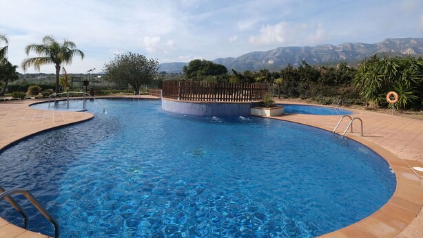 A pool with a wooden deck, a lifebuoy, and a view of mountains in the background. - Beautiful apartment for 4 people with pool, A/C, TV and terrace (Sant Carles De La Ràpita)