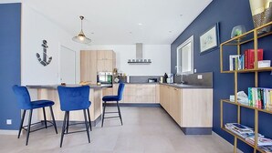 Une cuisine moderne dotée d’un îlot central, de tabourets de bar et d’une bibliothèque remplie de livres.