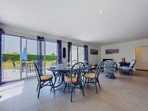 A spacious room with a dining table and chairs, large windows with curtains, and a flat-screen TV.