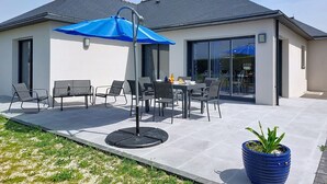 Une maison moderne dotée d’un patio, de mobilier d’extérieur et d’un parasol bleu.