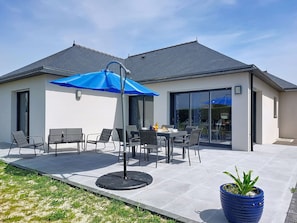 Une maison moderne dotée d’un patio, de mobilier d’extérieur et d’un parasol bleu.