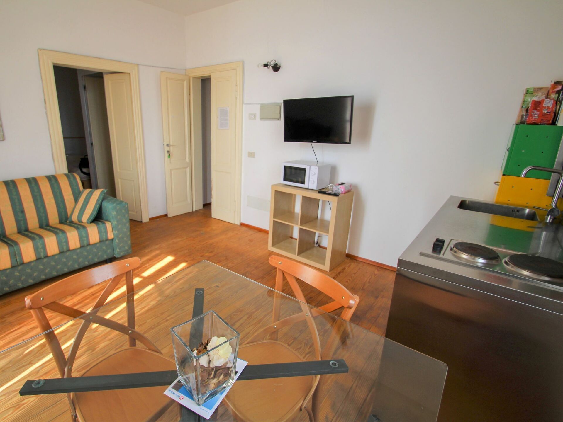 A living room with a sofa, a glass table with chairs, a television, a microwave, and a kitchen area with a sink.