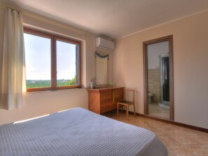 Une chambre à coucher comprenant un lit, une commode en bois, une chaise, une fenêtre donnant sur un paysage agréable et un espace douche.